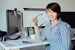 Portrait of Smiling Mixed race Woman holding eyeglasses during work at her home office workplace. Satisfied with work