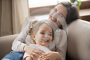 Portrait of smiling mom and little daughter relaxing on couch