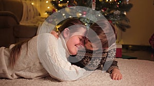 Portrait of smiling mom with son embracing and lying on carpet under Christmas tree in living room. Pure emotions of