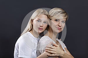 Portrait of a smiling mother with an adult daughter in light T-shirts on a black background. Women hug. Love, tenderness and