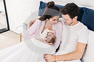 Portrait of smiling mother breastfeeding little baby with husband near by on bed
