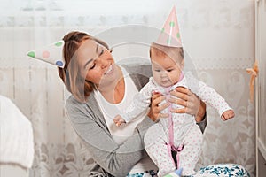 Portrait of a smiling mother and a cute baby who has a birthday party. Holiday hats on their heads. The concept of motherhood and