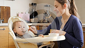 Portrait of smiling mother feeding her baby son with porridge from spoon. Concept of parenting, healthy nutrition and baby care