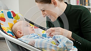 Portrait of smiling mother looking at her cute baby son sitting in electric rocking chair. Child development and happy