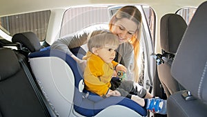 Portrait of smiling mother seating her toddler son in car safety seat