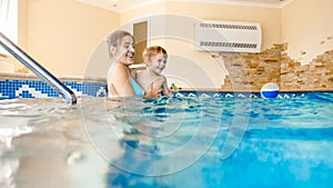 Portrait of happy smiling mother with 3 years old little son swimming in the pool at gym. Family raelaxing, having fun