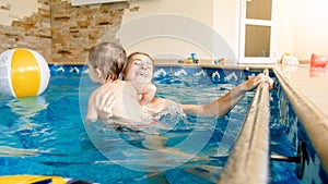 Portrait of happy smiling mother with 3 years old little son swimming in the pool at gym. Family raelaxing, having fun