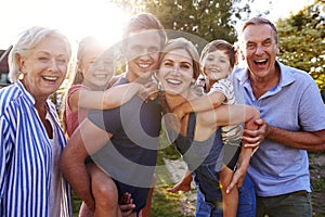 Portrait Of Smiling Multi Generation Family Outdoors In Summer Park Against Flaring Sun