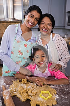 Portrait of smiling multi-generation family standing by dough in kitchen