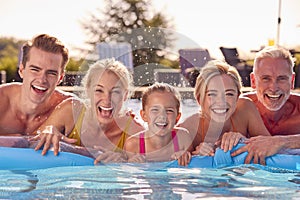 Portrait Of Smiling Multi-Generation Family On Summer Holiday Relaxing In Swimming Pool On Airbed