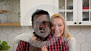 Portrait smiling multiethnic couple hugging looking camera at home kitchen