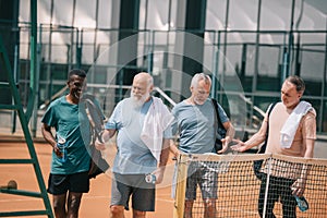 portrait of smiling multiracial elderly friends with tennis equipment