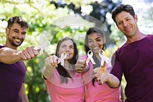 Portrait of smiling multiracial men and women showing breast cancer awareness ribbons in park