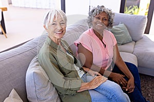 Portrait of smiling multiracial senior female friends sitting on sofa in living room at nursing home