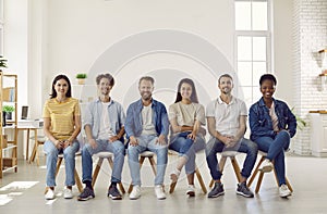 Portrait of smiling multiracial young people in casual clothes sitting in row on chairs.