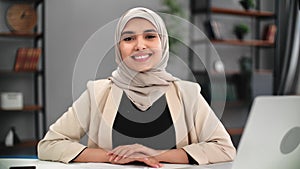 Portrait smiling Muslim business woman in hijab posing at workplace laptop desk modern home office