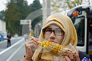 Portrait of smiling muslim woman eating roasted sweet corn smiling and happy expression.