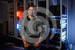 Portrait of smiling network engineer standing with laptop in server room