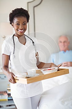 Portrait of smiling nurse with breakfast in tray while senior man lying on bed