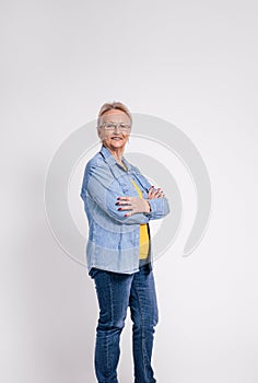 Portrait of smiling old businesswoman in eyeglasses and with arms crossed posing on white background