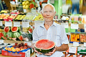 Portrait of smiling older man choosing sweet ripe fruits in farmer market