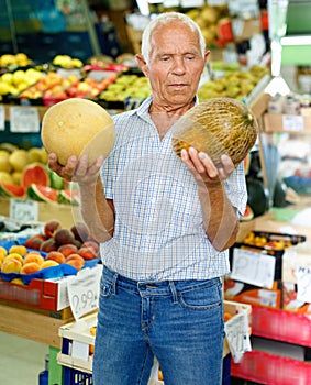 Portrait of smiling older man choosing sweet ripe fruits in farmer market