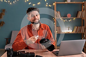 Portrait of smiling photographer holding Memory card - Flash card while sitting at the table with professional DSLR