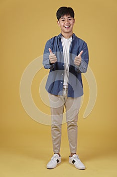 Portrait of smiling positive young asian man dressed casually with thumb up gesture approving expression isolated on yellow
