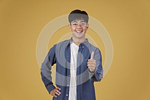 Portrait of smiling positive young asian man dressed casually with thumb up gesture approving expression isolated on yellow