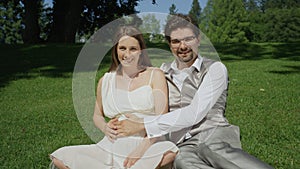 PORTRAIT: Smiling pregnant couple caressing her pregnant belly in sunlit park