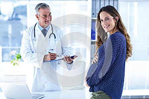 Portrait of smiling pregnant woman with male doctor in clinic