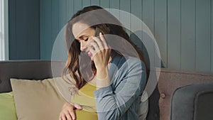 Portrait of smiling pregnant woman talking smartphone on couch at modern home.