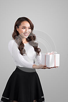 Portrait of a smiling pretty asian woman holding gift box isolated over gray background
