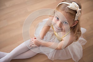 Portrait of smiling pretty diligent ballet girl sitting in white