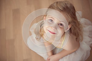 Portrait of smiling pretty diligent ballet girl sitting in white photo