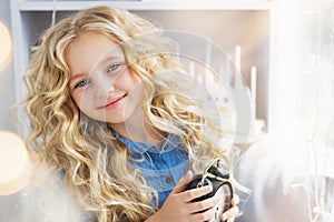 Portrait of smiling pretty little girl with a clock at hands near the window