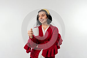 Portrait of smiling pretty woman keeping mug with beverage wearing red sweater, standing over white background