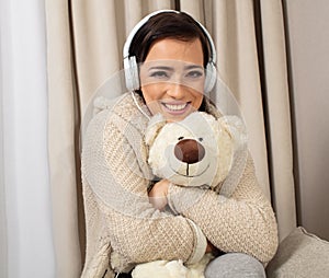 Portrait of a smiling pretty woman posing with headphones and teaddy bear