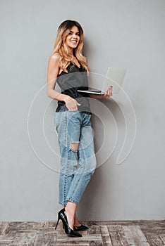 Portrait of a smiling pretty woman standing and holding laptop