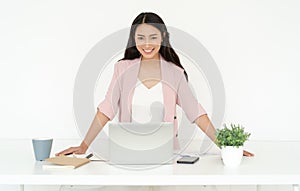 Portrait of smiling pretty young Asian business woman working small business online standing at workstation of desk and looking at