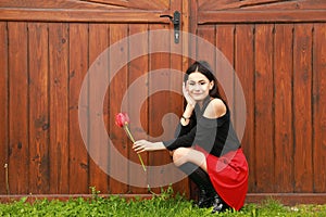 Portrait of smiling pretty young teen girl with red tulip by gate