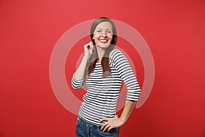 Portrait of smiling pretty young woman in casual striped clothes standing keeping hand near head isolated on bright red