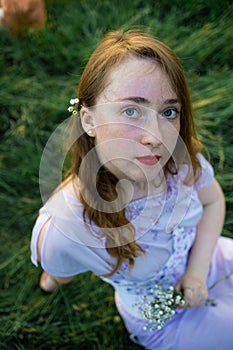 Portrait of a smiling red head girl with long hair resting on green grass in summer park.