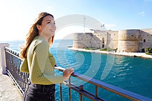 Portrait of smiling relaxed traveler woman looking Taranto city from seafront, Apulia, Italy photo