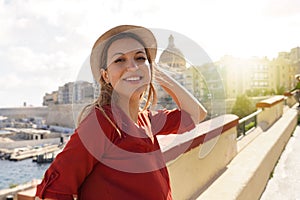 Portrait of smiling relaxed traveler woman walking along Valletta seafront, Malta