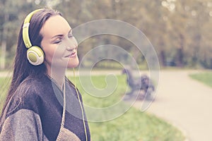 Young happy woman listening music from smartphone with headphones in a quiet Park