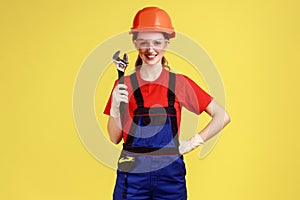 Builder woman holding adjustable wrench, looking at camera with happy facial expression.