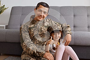 Portrait of smiling satisfied young adult soldier man wearing camouflage uniform returning home after army, spending time with