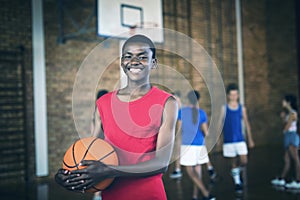 Smiling school boy holding a basketball while team playing in background