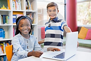 Portrait of smiling school kids using a laptop in library